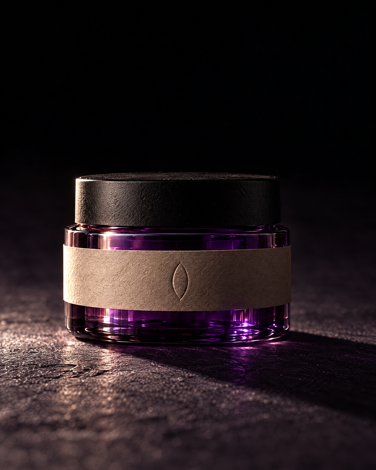 The almond balm jar lit from one side on dark stone, the glass glowing from within